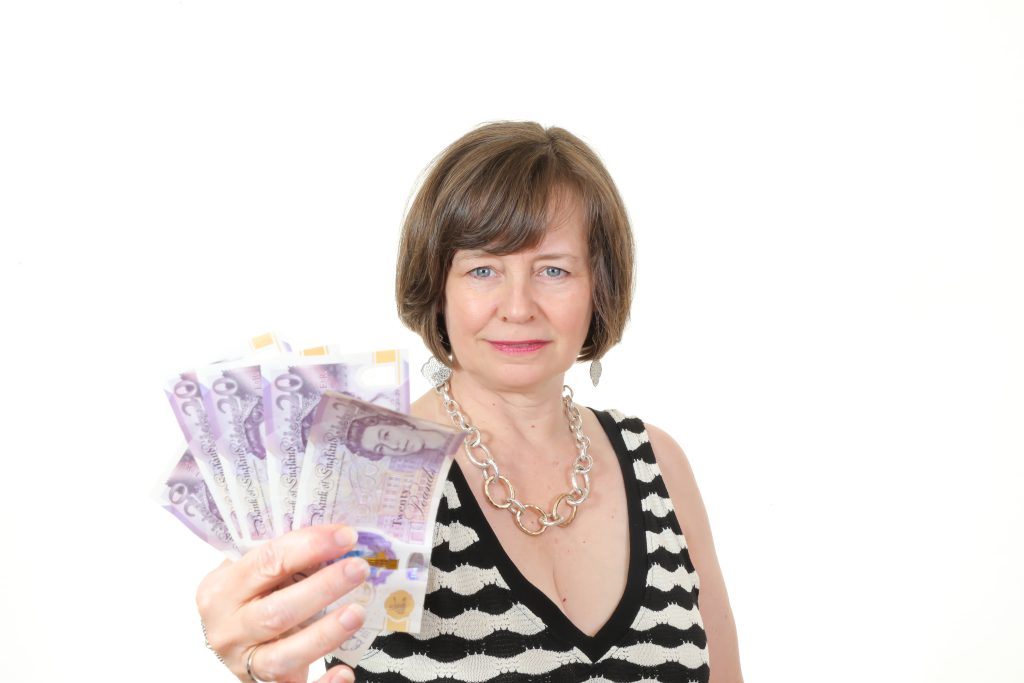 A female working in financial copywriting in a black and white checked dress against a white background holding £20 notes.